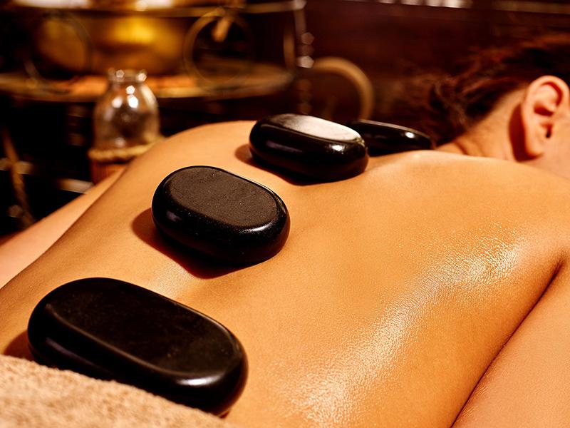 Massage Đá Nóng Thư Giãn Sâu Khách hàng nằm thư giãn trong liệu pháp massage đá nóng với các viên đá bazan ấm đặt dọc sống lưng